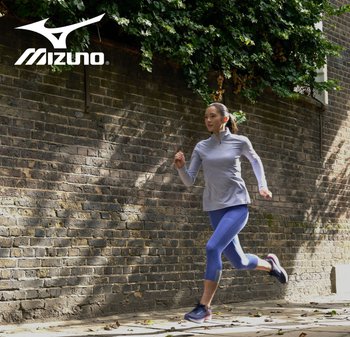 Ropa de running que incluye una camiseta de cremallera gris claro y leggings azules. El conjunto se complementa con zapatillas de running oscuras sobre un camino de ladrillos.