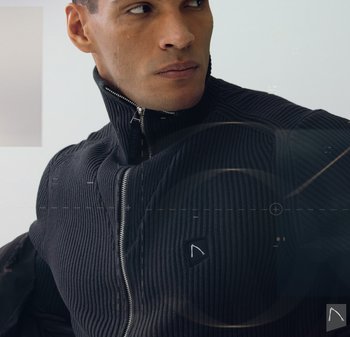 Zwarte geribbelde zip-up trui met hoge kraag, voorzien van een klein logopatch op de linkerborst en een zilveren ritsdetail.