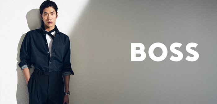 Dunkelblaue Jeanshemd mit Knöpfen und hochgekrempelten Ärmeln, kombiniert mit einem weißen T-Shirt und hoch taillierten schwarzen Hosen. Auffällige Marke: „BOSS“.