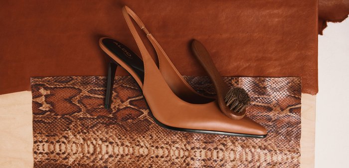 Brauner Leder-High-Heel-Slingback-Schuh mit einer Schuhbürste, die auf der spitzen Schuhspitze liegt, auf einem stoff mit Schlangenmuster platziert.