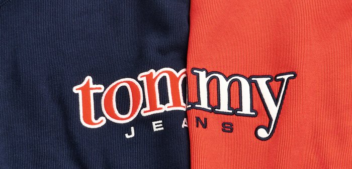 Tela de algodón azul marino y roja con el destacado logo "tommy jeans". Texto en blanco y naranja, con textura acanalada y colores contrastantes.
