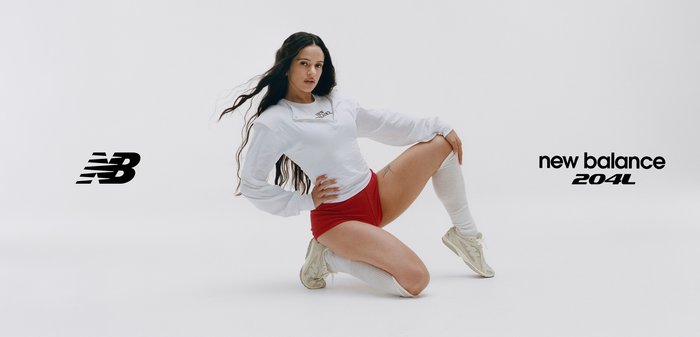 Femme portant un sweat-shirt blanc, un short rouge, des chaussettes montant aux genoux et des baskets blanches New Balance, posant à genoux devant un fond uni.