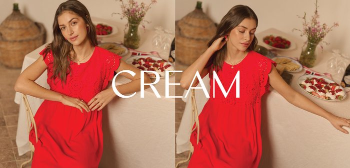 Giovane donna in abito rosso seduta accanto a un tavolo con formaggio, cracker e frutta, che sorride dolcemente in una stanza illuminata soffusamente.