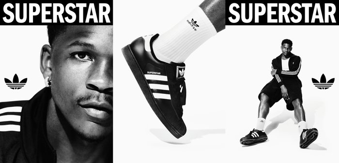 Sneakers Adidas Superstar neri con strisce bianche, suola in gomma nera e marchio "SUPERSTAR". Presentati con calzini bianchi e abbigliamento sportivo.