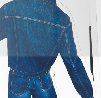Persona che indossa una giacca di jeans blu e jeans abbinati, in piedi con la schiena rivolta verso la fotocamera su uno sfondo bianco.