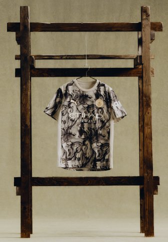 Manchester City voetbalshirt met zwart-wit abstract patroon, hangend aan een houten frame tegen een beige achtergrond.