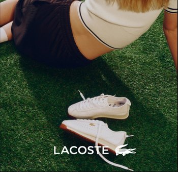 Mujer acostada sobre el césped con shorts negros y camiseta blanca, con zapatillas blancas de Lacoste colocadas cerca sobre el césped.