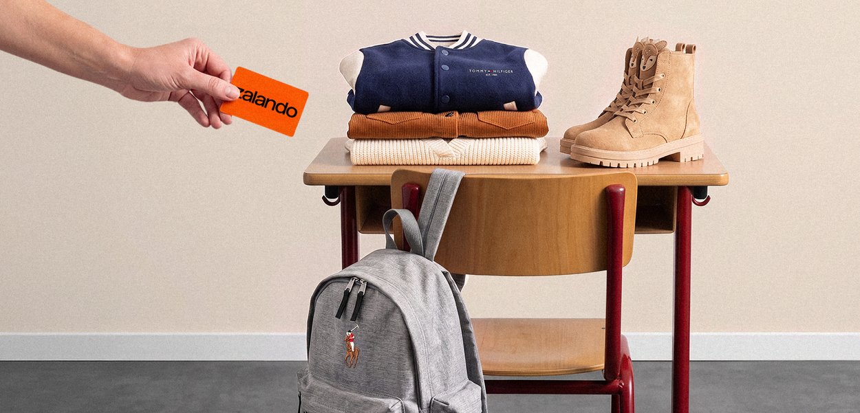 Hand houdt een oranje Zalando-kaart vast bij een schoolbank met opgevouwen kleren, beige laarzen en een grijze rugzak die aan de stoel hangt.