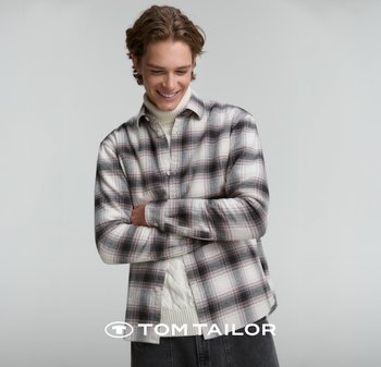 Koszula flanelowa w kratę w odcieniach bieli, czerni i czerwieni. Posiada zapięcie na guziki z przodu oraz długie rękawy. Nosi się ją na kremowym swetrze.