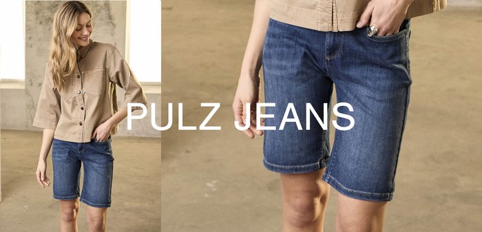 Oseba, oblečena v modre jeans kratke hlače do sredine stegnenice in bež srajco s kratkimi rokavi z gumbi, z roko v žepu.