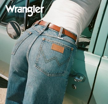 Person som har på seg blå Wrangler-jeans med et brunt belte og lener seg inn gjennom det åpne vinduet på en lys grønn veteranbil.