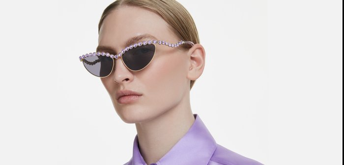 Vrouw met kattenoogzonnebril versierd met paarse steentjes en een glanzend lavendelkleurig overhemd met een brede kraag.