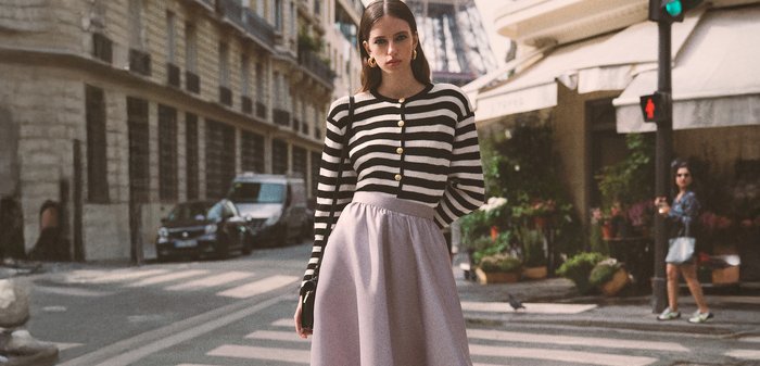 Cardigan rayé noir et blanc avec des boutons dorés, associé à une jupe fluide lavande, se tenant dans une rue avec la Tour Eiffel en arrière-plan.