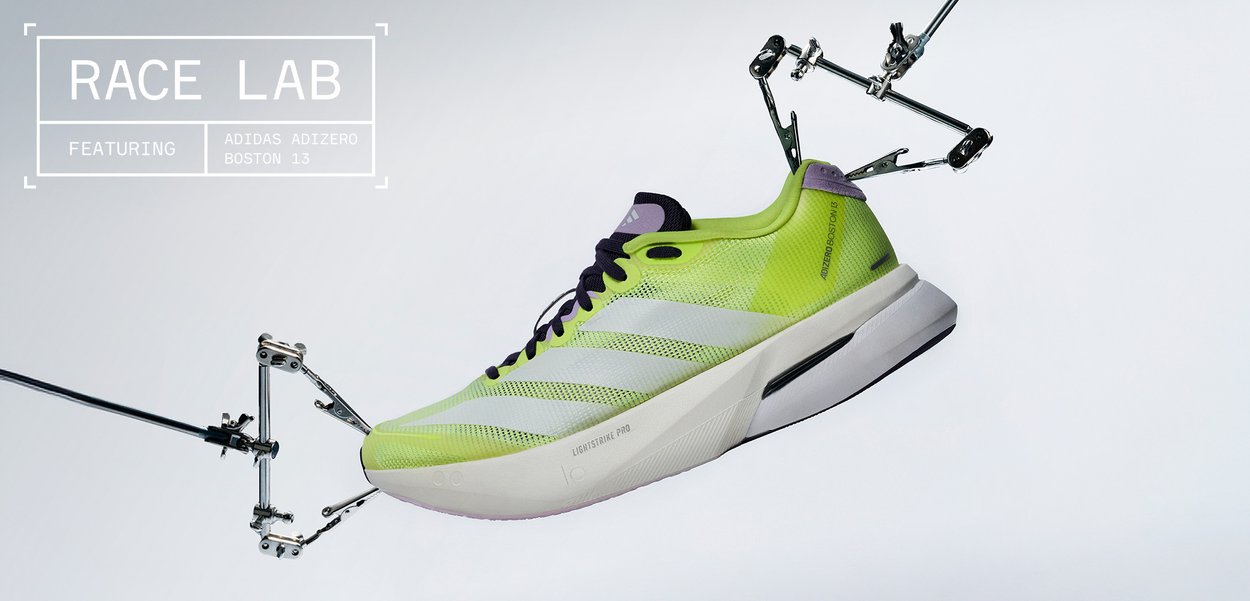 Yellow-green Adidas Adizero Boston 13 running shoe suspended by mechanical clamps against a white background.