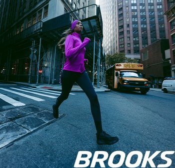 Hardloopkleding in roze stof, gecombineerd met zwarte leggings. Stedelijke omgeving met een gele schoolbus en steigers op de achtergrond.