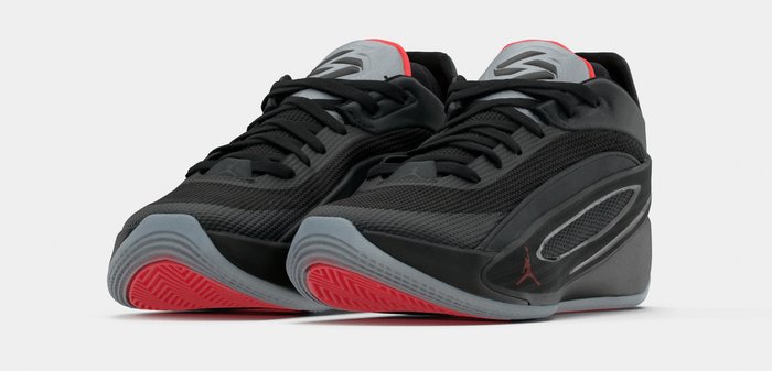 Ζευγάρι μαύρα αθλητικά παπούτσια χαμηλού προφίλ με γκρι και κόκκινες σόλες, δίχτυα και κορδόνια, γερμένα προς τα εμπρός σε λευκό φόντο.