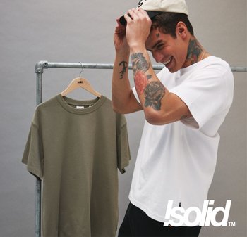 Weißes Baumwoll-T-Shirt vor einem grauen Hintergrund, daneben ein grünes T-Shirt, das an einem Metallgestell hängt. Mit rundem Ausschnitt und kurzen Ärmeln.