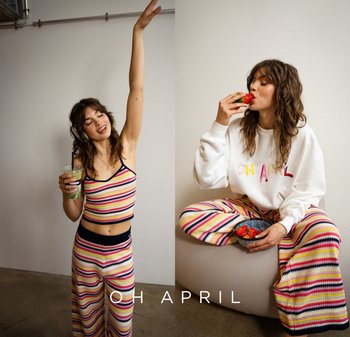 Gestreifter Strick-Crop-Top und weit geschnittene Hose in Pastellfarben, kombiniert mit einem weißen Sweatshirt. Die Person hält ein Getränk und eine Schüssel mit Erdbeeren.