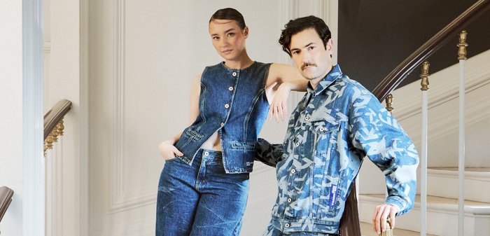 Femeie în vestă fără mâneci din denim și blugi largi stând pe scări lângă un bărbat în jachetă din denim cu model și pantaloni scurți, sprijinit de balustradă.