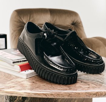 Chaussures en cuir verni noir avec une semelle en caoutchouc striée et un design à lacets. Présentent une étiquette de marque sur le côté et une finition lisse et brillante.