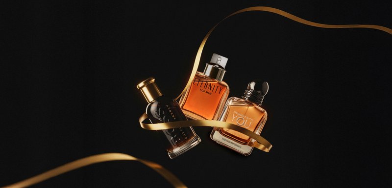 Trois flacons de parfum : un flacon noir avec un capuchon en or, un flacon ambre avec une buse en argent, et un flacon ambre transparent avec un cap arrondi, enveloppé dans un ruban doré.