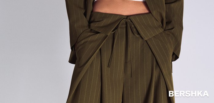 Pantaloni evazați verzi măsliniu cu dungi subțiri, cu detaliu cu fundă în față, asortați cu un blazer scurt de aceeași nuanță.