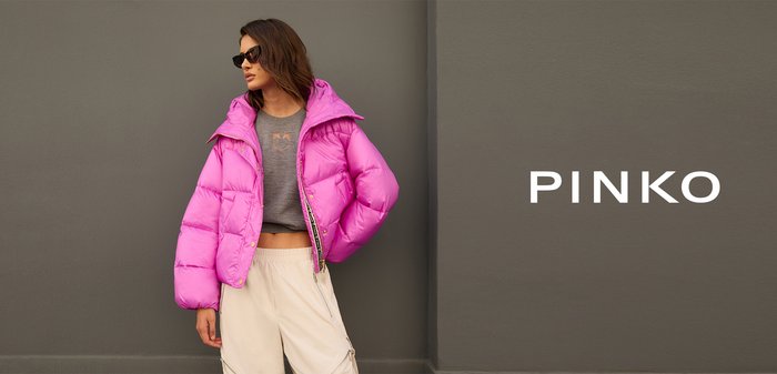 Pink padded jacket with a high collar, shiny texture, and zip closure; worn over a gray top and paired with light-colored trousers.