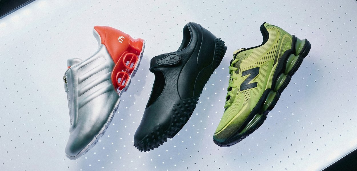 Three different sports shoes in silver with orange, black, and green placed side by side on a white perforated surface.