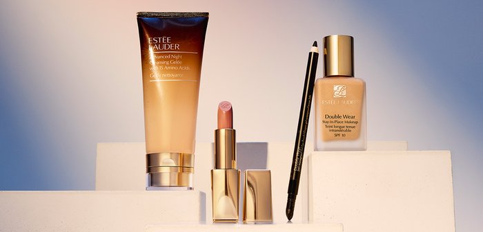 Produits de soins de la peau et de maquillage Estée Lauder : emballages dorés et transparents, un gel nettoyant brun, un rouge à lèvres rose, un fond de teint liquide et un crayon noir.