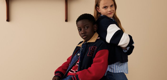 Zwei Kinder posieren zusammen und tragen eine rot und marineblau gemischte Jacke mit beigem Kragen sowie ein marineblaues Oberteil mit weißen Streifen.