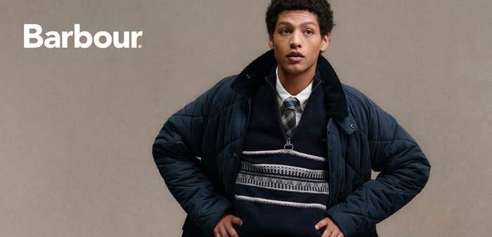 Marineblaue gesteppte Jacke mit hohem Kragen, darüber ein dunkler Pullover mit geometrischem Muster; dunkelgraue Hose und schwarzer Gürtel.