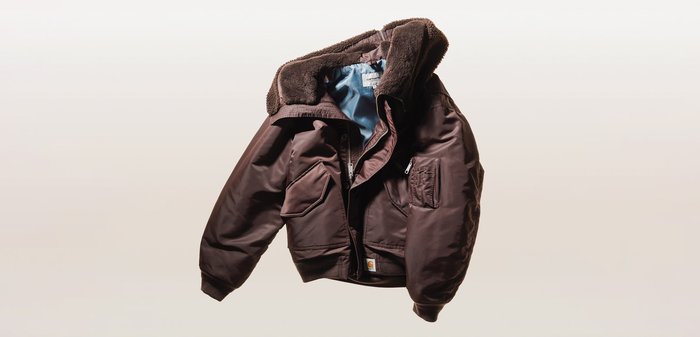 Chaqueta bomber marrón aislada con cuello de piel, cierre de cremallera y botones, múltiples bolsillos y forro interior azul claro.