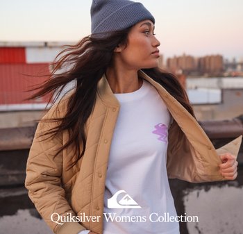 Veste bomber matelassée couleur tan avec des boutons-pression sur un t-shirt blanc portant un logo rose et un bonnet en tricot gris. De longs cheveux ondulés tombent librement.