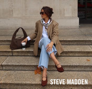 Bruine schoudertas, witte shirt, beige blazer, lichtblauwe jeans met rafelige onderkant, en bordeaux flats. Sjaal om de nek. Koffiemok in de hand.