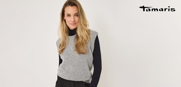 Grau ärmelloser Pullover aus weichem Material mit rundem Ausschnitt, über einem schwarzen Langarmshirt getragen. Glatte Textur, lässiges Design.