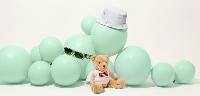 Klynge med mintgrønne ballonger, der en har på seg solbriller og hatt, og en bamse i genser som sitter foran.