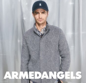 Gray knitted sweater with diamond pattern, featuring a high collar, paired with a blue cap displaying a ribbon logo. Background is draped gray.