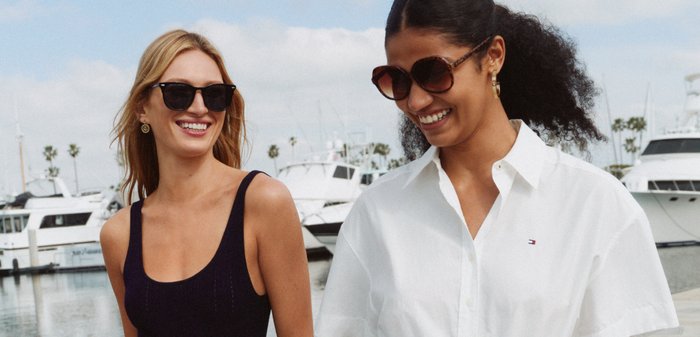 Deux femmes portant des lunettes de soleil sourient en marchant près de bateaux amarrés dans une marina.