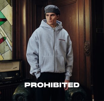 Young man wearing a gray zip-up hoodie and gray beret, standing indoors near stained glass and vintage radio, with "PROHIBITED" text below.