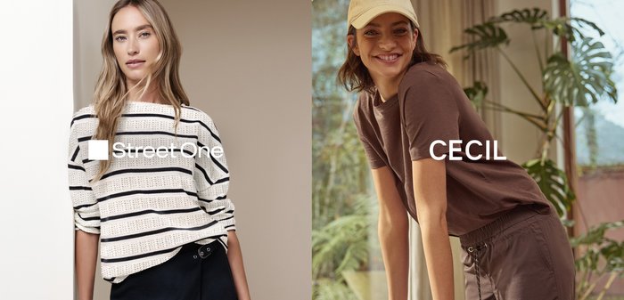 Nainen raidallisessa neulepaidassa ja mustassa hameessa seisoo hymyilevän naisen vieressä, joka pukeutunut ruskeaan rentoon asuun ja beigepäähineeseen, nojaten puupöytään.