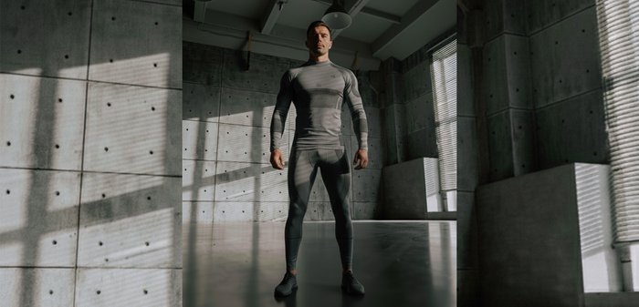 Grijs sportief outfit met lange mouwen en een aansluitend ontwerp, voorzien van horizontale strepen en gestructureerde panelen, geplaatst in een industriële ruimte.