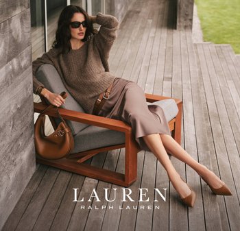 Maglione marrone a maglia, gonna midi taupe e décolleté beige a punta. Borsa marrone morbida, sedia di legno e cuscino grigio su un patio in legno.