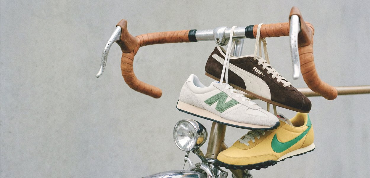 Τρία ζευγάρια αθλητικά παπούτσια κρέμονται από τα κορδόνια τους σε καφέ δερμάτινα ριγμένα τιμόνια ενός ρετρό ποδηλάτου με φόντο γκρι.