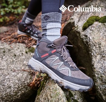 Graue Wanderschuhe mit roten Akzenten und einer strukturierten Oberfläche, auf steinigem Gelände platziert. Knöchelhoch mit gedämpfter Sohle und sichtbarem Logo.