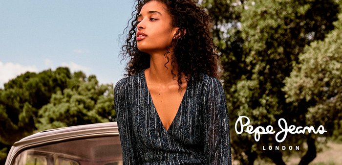 Abito avvolgente blu scuro con righe verticali argento, maniche lunghe, scollatura a V profonda e un leggero luccichio, abbinato a capelli ricci contro uno sfondo naturale.