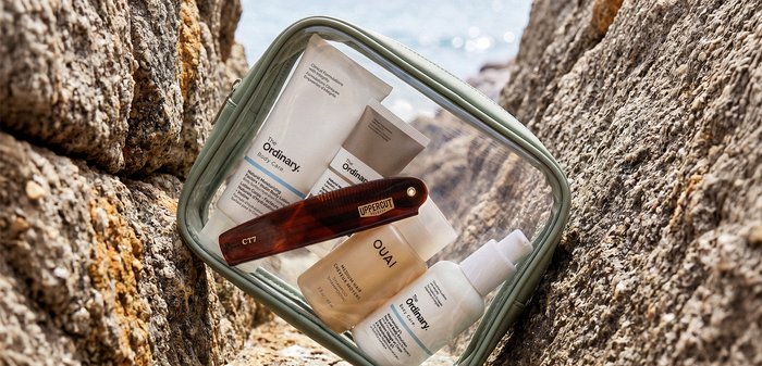 Petit miroir posé sur des rochers reflétant des produits de soins de la peau de The Ordinary et OUAI, à côté d'un rasoir droit en bois étiqueté Uppercut.