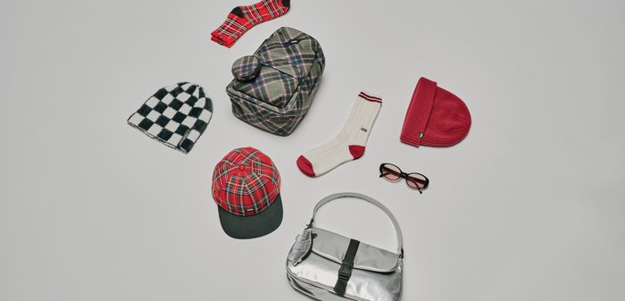 Collezione di accessori che include uno zaino a quadri, un berretto a quadri rosso, un berretto lavorato a maglia a quadri, calzini bianchi con accenti rossi e una borsa metallizzata.