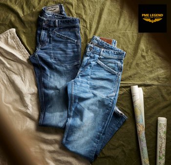 Twee opgevouwen blauwe spijkerbroeken liggend op een groen en beige stuk stof met twee opgerolde landkaarten ernaast en het PME Legend-logo rechtsboven.