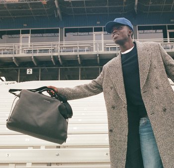 Sac à main en cuir noir avec deux poignées et une bandoulière amovible, présentant une texture lisse et un design minimaliste.