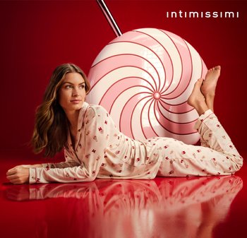 Langärmeliges, helles Pyjama-Set mit kleinen Blumenmustern, kombiniert mit einem großen rosa-weißen Spiral-Lutscher vor rotem Hintergrund.